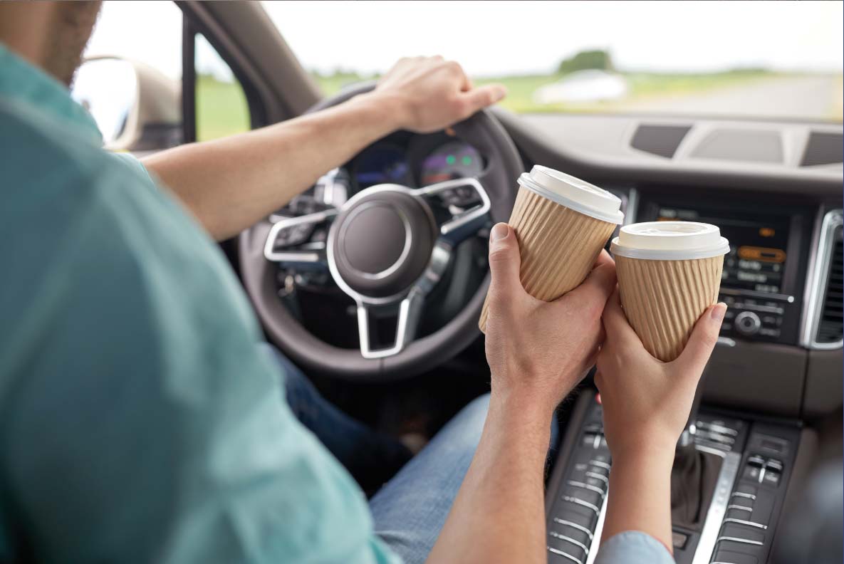 Image of a couple in a car toasting with two takeout coffee cups