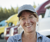 Image captures a young female truck driver confidently standing in front of a fleet of trucks