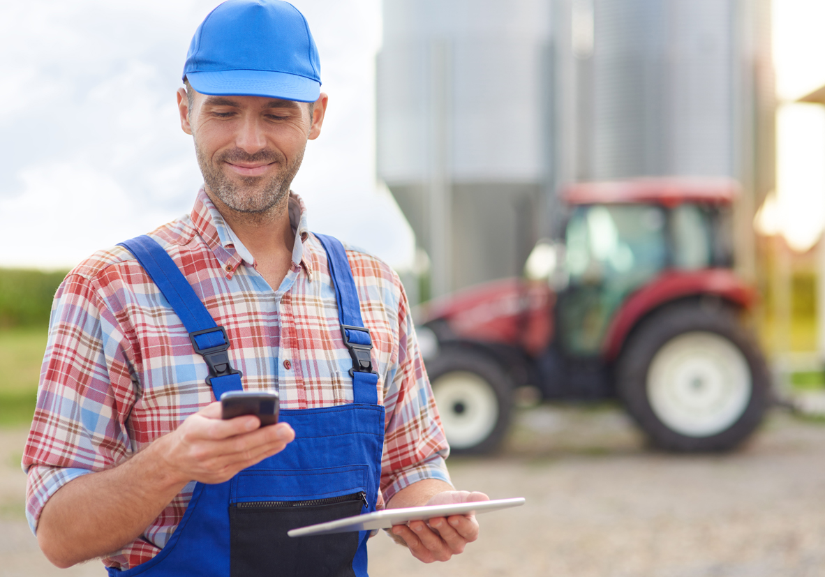 Image of a male farmer on his cell phone standing on his farm yard