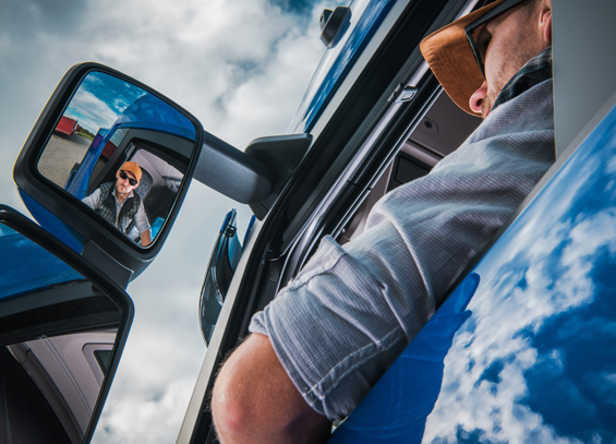 Image of a young man driving a truck while looking in his driver side mirror